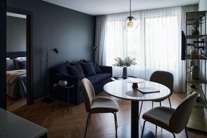 A modern living room with a dark blue sofa, a round dining table with chairs, a floor lamp, and a bookshelf. - Innapartments Avenida 60 (Aveiro)