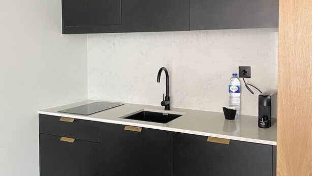 A modern kitchen with black cabinets, a white countertop, a black sink, and a water bottle on the counter. - Innapartments Avenida 60 (Aveiro)