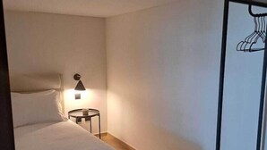 A hotel room with a bed, bedside table, lamp, and a clothing rack. - Innapartments Avenida 60 (Aveiro)