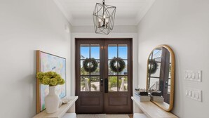 A hallway with a double door, a mirror, a vase with flowers, and a painting on the wall. - Wagon Wheeler 6 Bed 4 Bath Private Pool Close to Gulf & Village Sleeps 12 (Boca Grande)