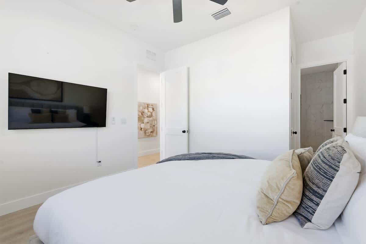 Une chambre moderne avec un grand lit, un téléviseur à écran plat fixé au mur et une porte donnant sur une autre pièce.