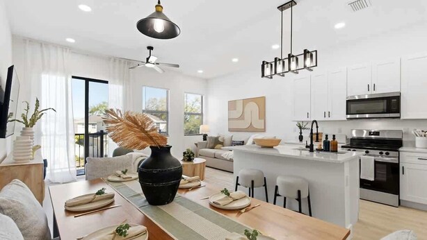 Une cuisine moderne avec des meubles blancs, un îlot central et un coin repas agrémenté d’une longue table dressée pour quatre personnes.