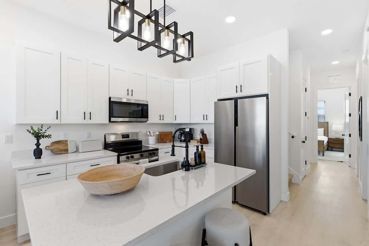 Una cocina moderna con armarios blancos, electrodomésticos de acero inoxidable, una isla central y una lámpara colgante geométrica única.