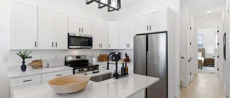 Una cocina moderna con armarios blancos, electrodomésticos de acero inoxidable, una isla central y una lámpara colgante geométrica única.