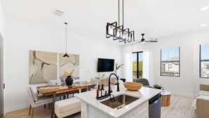 Une cuisine moderne dotée d’un îlot central, un coin repas avec une table et des chaises, et un espace de vie comprenant un canapé et un téléviseur.