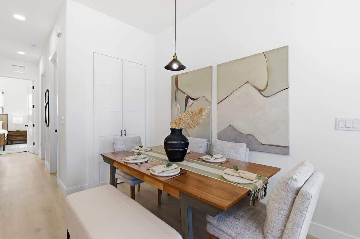 A dining area with a wooden table set for four, a vase with dried plants, and abstract wall art.