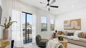 Un salon moderne avec un canapé, un fauteuil et une table basse, de grandes fenêtres et un ventilateur de plafond.