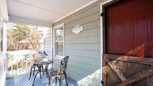 Un portico coperto con tavolo e sedie, un'anta di garage rossa e un cartello con scritto 'Peachy'.