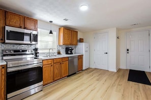 Una cocina con armarios de madera, electrodomésticos de acero inoxidable, encimera negra y una puerta blanca.