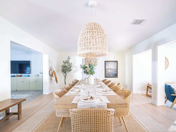 Un comedor con una mesa larga, sillas de mimbre y una lámpara colgante.