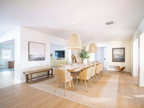 Un comedor amplio con una larga mesa de madera, sillas de mimbre e iluminación colgante de fibra.