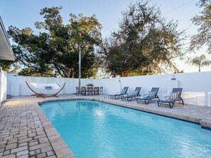 Una piscina con sillas de descanso y una mesa, rodeada por una cerca blanca y árboles.