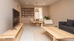 A modern living room with a sofa, a TV, a dining table with chairs, a bookshelf, and a hanging light fixture. - LUMEN - Loft Modern Downtown GDL | Gym & Coworking (Guadalajara)