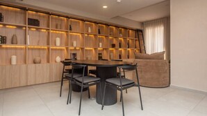 A modern dining area with a round table, four chairs, a sofa, and a wooden bookshelf with shelves. - LUMEN - Loft Modern Downtown GDL | Gym & Coworking (Guadalajara)