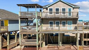 Una casa fronte mare a più piani con un balcone, un pontile in legno e terreno sabbioso.