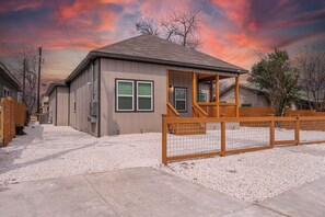 A single-story building with a covered porch, a fenced yard, and a gravel driveway. - Sleek 3 Bedroom /2 Bath Just 5 Minutes to Downtown (San Antonio)