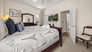 Un dormitorio con cama, una silla, ventilador de techo, un cuadro y una ventana.