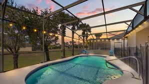 Una piscina con zona cubierta, rodeada de árboles y vista al atardecer.