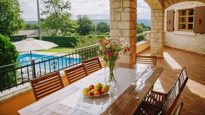 A stone patio with a pool, wooden benches, a table with fruit, and a vase of flowers. - Villa Vernier (Istria - Kringa) (Kringa)