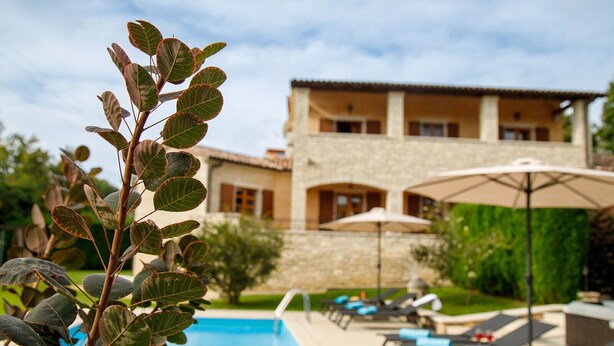 A poolside area with lounge chairs and umbrellas, a stone building with multiple windows, and a clear blue sky. - Villa Vernier (Istria - Kringa) (Kringa)