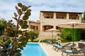 A poolside area with lounge chairs and umbrellas, a stone building with multiple windows, and a clear blue sky. - Villa Vernier (Istria - Kringa) (Kringa)