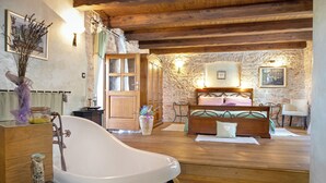 Una habitación con bañera, muebles de madera, paredes de piedra y una cama con cabecero.
