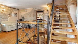 Una escalera con escalones de madera y barandillas de metal, un sofá blanco y una pared de piedra en una habitación con suelo de madera.