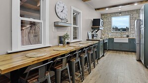 Una cocina con una mesa de madera, taburetes de bar, un reloj y una pared de piedra.