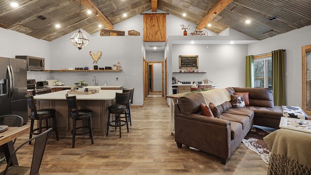 Una cocina amplia con una isla central, un comedor con sillas, un sofá de cuero marrón y un ventanal con cortinas.