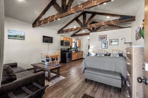 Quarto aconchegante com cama, sofá, mesa de jantar, cozinha e vigas de madeira no teto.