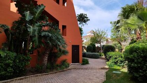 A courtyard with a paved walkway, surrounded by lush greenery and an orange building. - New Galera Gardens (Estepona)