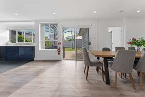 A modern kitchen with a built-in oven, a dining area with a wooden table and grey chairs, and a sliding glass door leading to a patio. - Birubi Beach Escape At Anna Bay (Anna Bay)