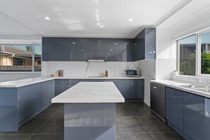 A modern kitchen with dark blue cabinets, a white marble countertop, and a built-in dishwasher. - Birubi Beach Escape At Anna Bay (Anna Bay)