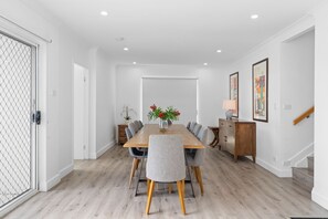 A dining room with a wooden table, grey upholstered chairs, and a vase with flowers. - Birubi Beach Escape At Anna Bay (Anna Bay)
