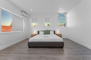 A modern bedroom with a large bed, two bedside tables, and three windows. - Birubi Beach Escape At Anna Bay (Anna Bay)