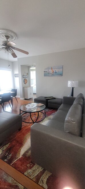 Un salon avec un canapé, une table basse, un ventilateur de plafond et un tableau accroché au mur.
