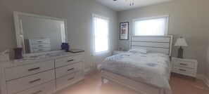 Une chambre à coucher comprenant un lit, une commode, une table de chevet, une lampe et un tableau encadré accroché au mur.