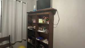 Ein Schlafzimmer mit Bett, Kleiderschrank, Fernseher auf einem Schrank und einem Fenster mit Vorhängen.