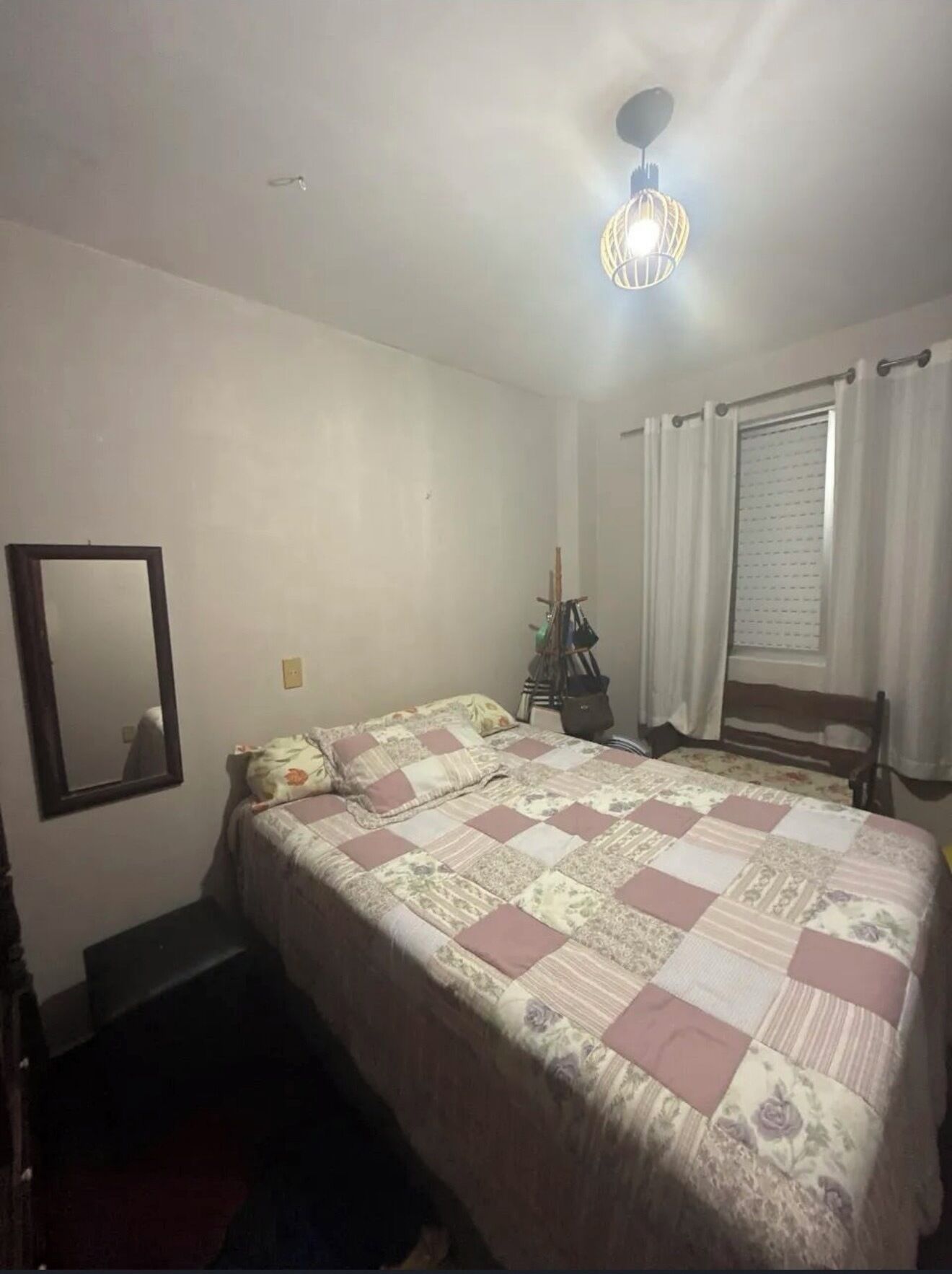 A bedroom with a bed, a mirror, a window with curtains, and a ceiling light fixture.