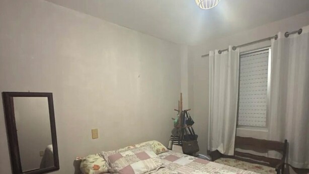 Ein Schlafzimmer mit Bett, Spiegel, einem Fenster mit Vorhängen und einer Deckenleuchte.