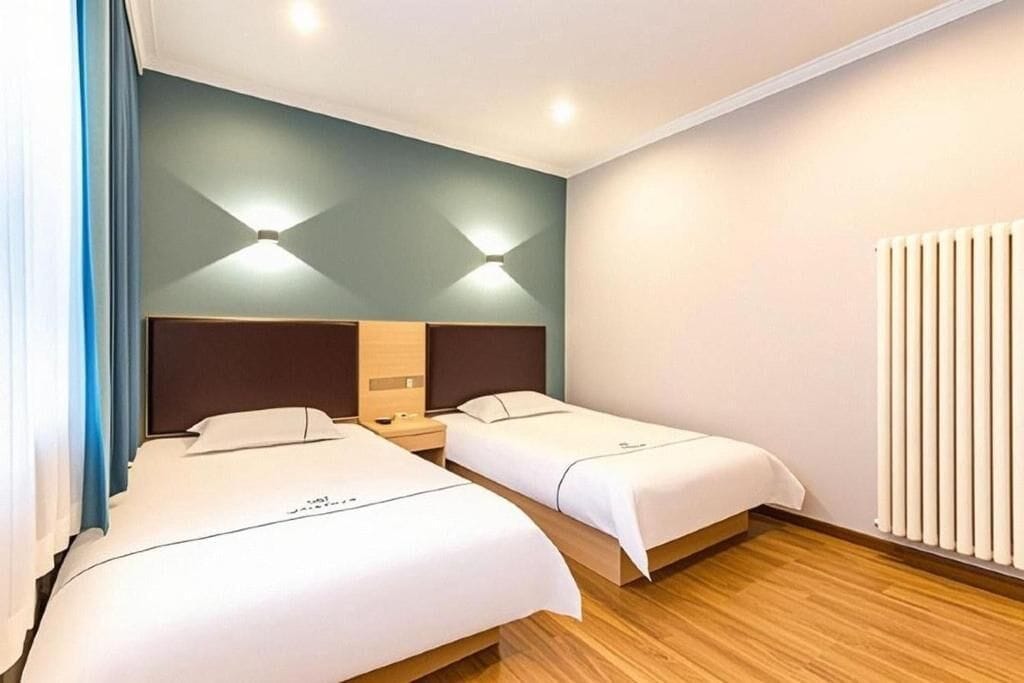 Een hotelkamer met twee bedden, een houten vloer, een radiator aan de muur en een plafondlamp.