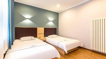 Een hotelkamer met twee bedden, een houten vloer, een radiator aan de muur en een plafondlamp.