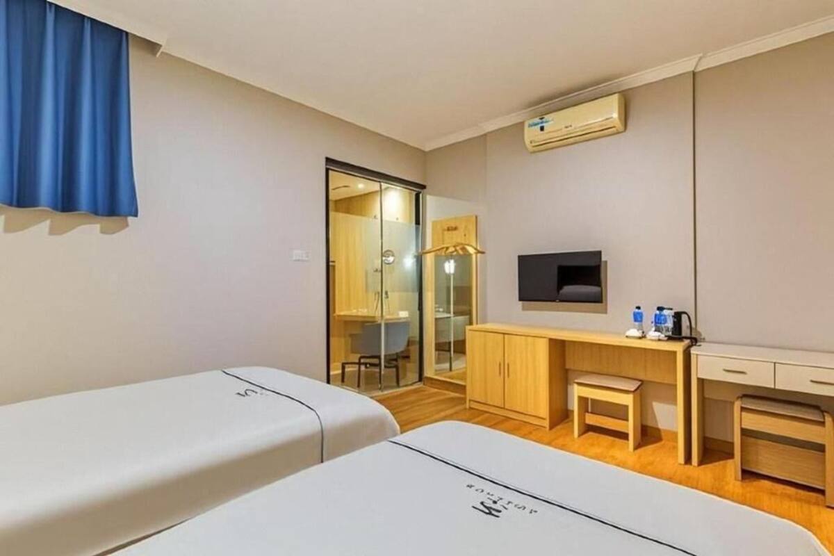 A hotel room with two beds, a desk, a chair, a TV, and an air conditioning unit.