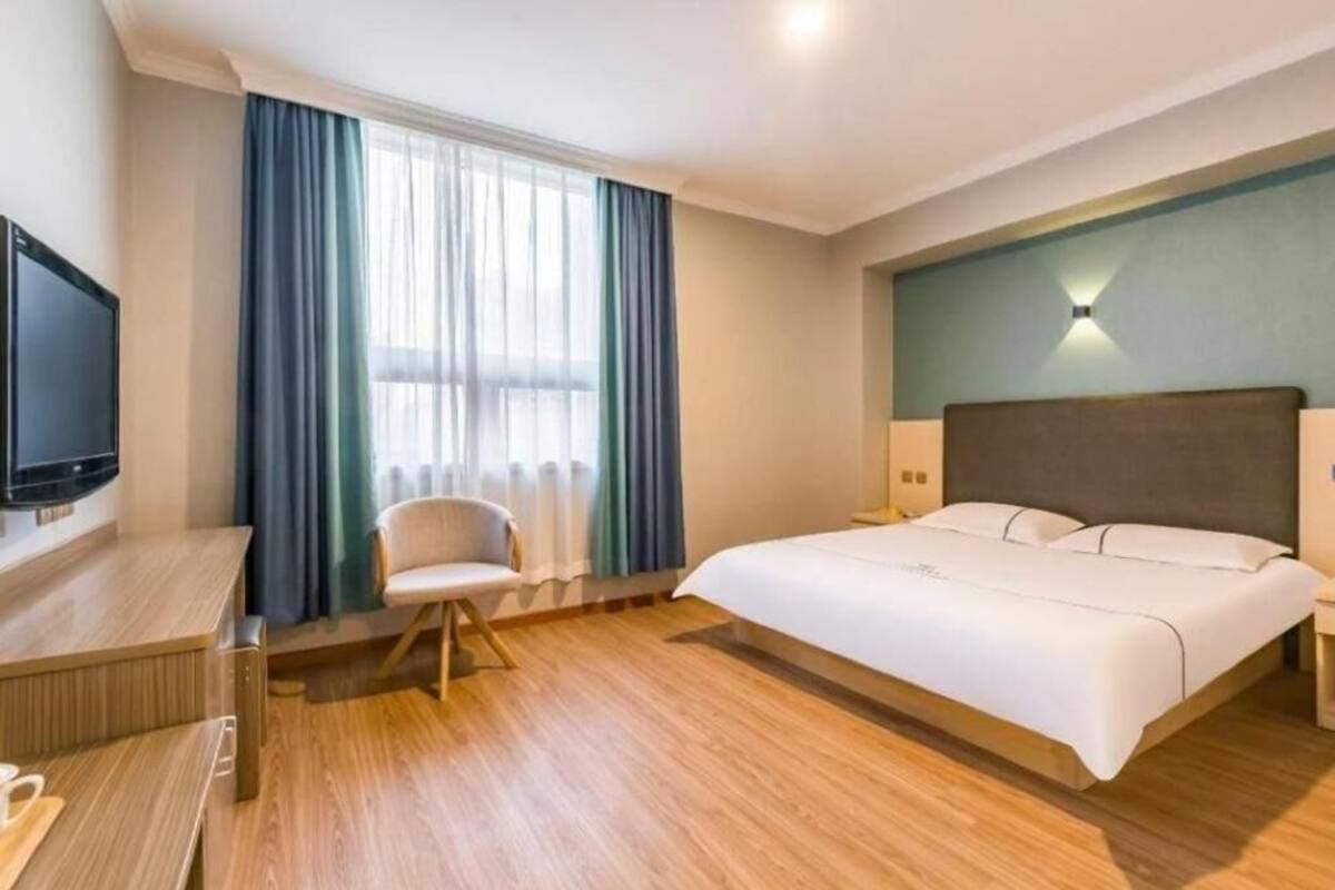 A hotel room with a bed, a desk, a chair, a TV, and a window with curtains.