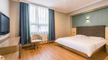 Ein Hotelzimmer mit Bett, Schreibtisch, Stuhl, Fernseher und einem Fenster mit Vorhängen.