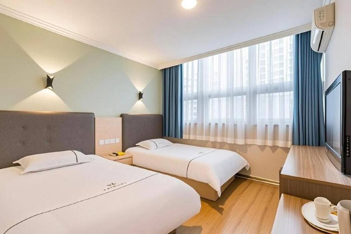 A hotel room with two beds, a desk with a TV, and a window with curtains.