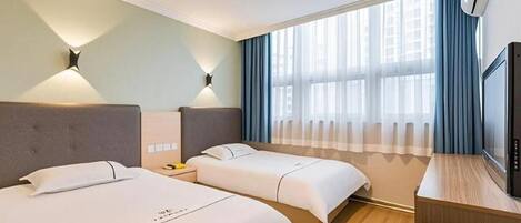 Una camera d'albergo con due letti, una scrivania con televisione e una finestra con tende.