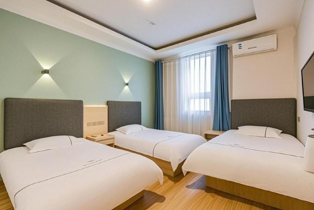 A hotel room with three beds, a TV, an air conditioner, and a window with curtains.