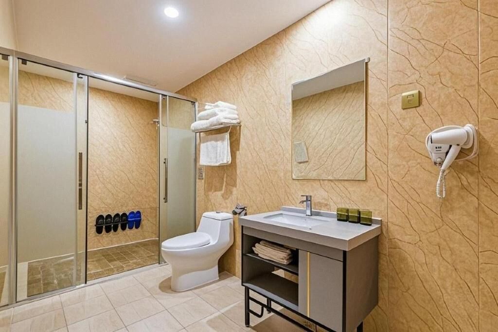 A modern bathroom with a glass shower enclosure, a toilet, a sink with a mirror, and a hairdryer on the wall.