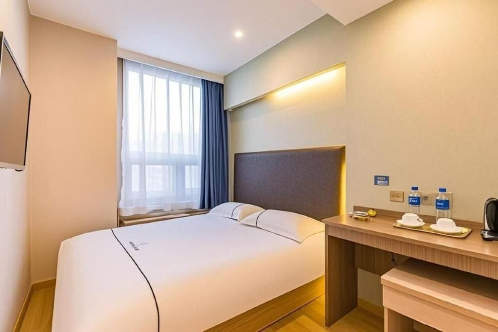 Une chambre d’hôtel avec un lit, un bureau avec un téléphone, un miroir et une fenêtre avec des rideaux.